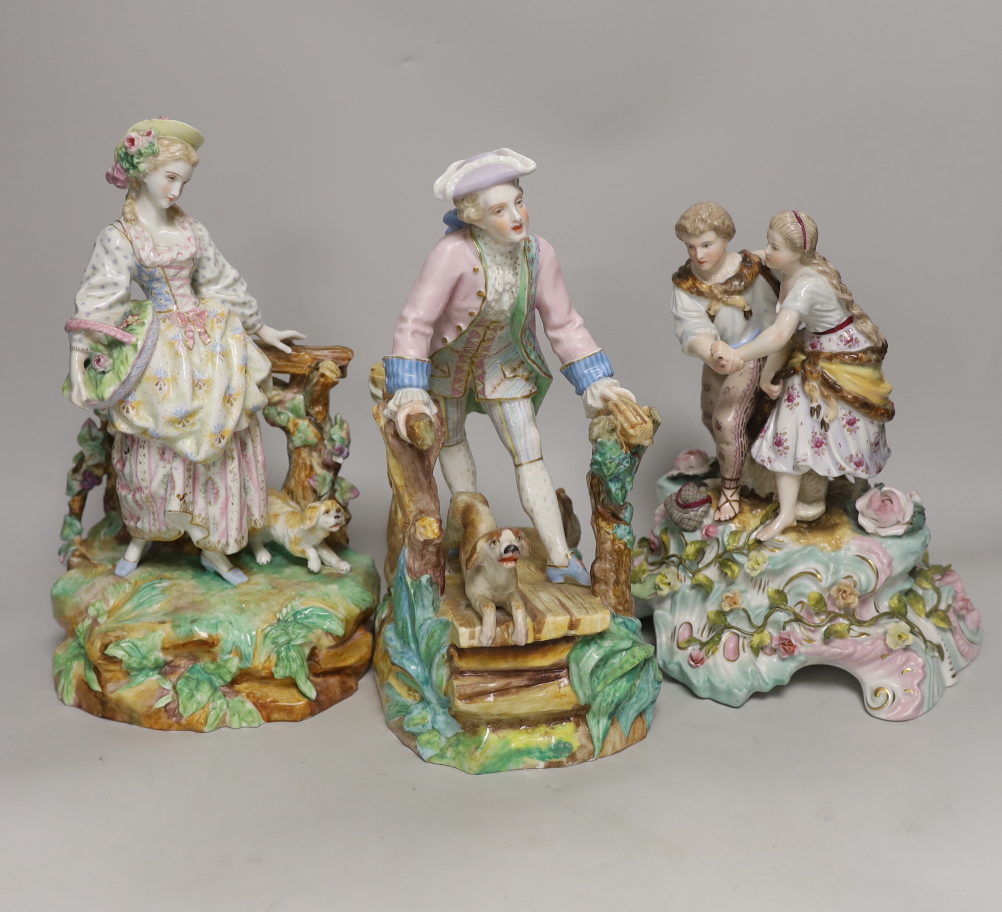 Three German porcelain figures including a Sitzendorf group of a young couple and a sheep, together with a pair of lovers with dogs, highest 28cm